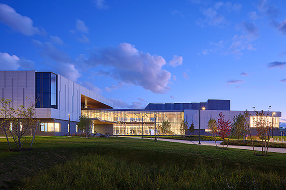 Modern building exterior at dusk with landscaped surroundings and cloudy sky.