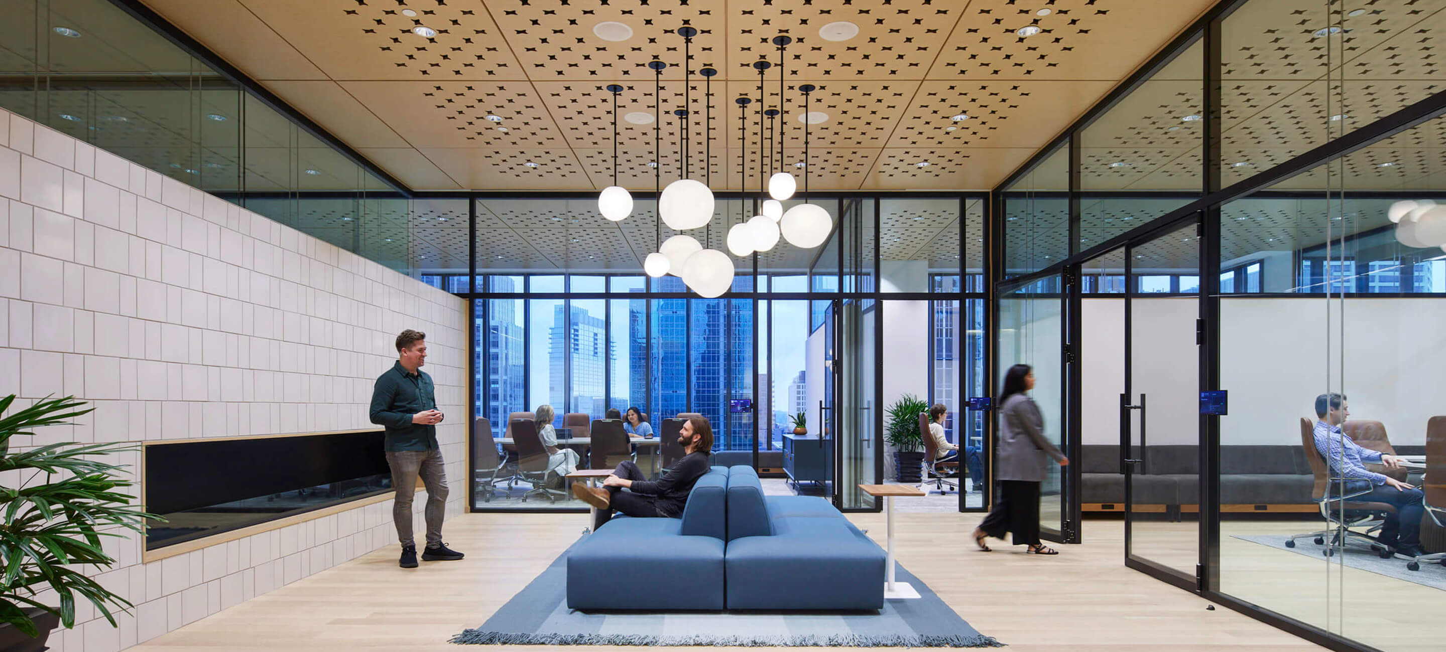 Modern office interior with glass walls, stylish furniture, and people engaged in conversation.