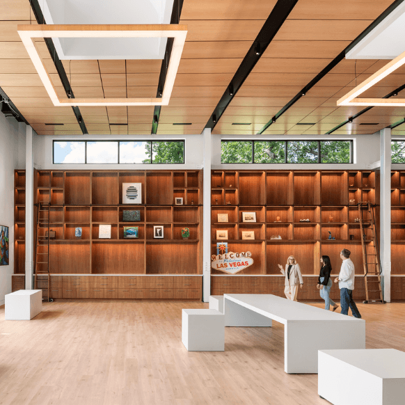 Modern gallery with wooden shelves, art displays, and visitors exploring the space.