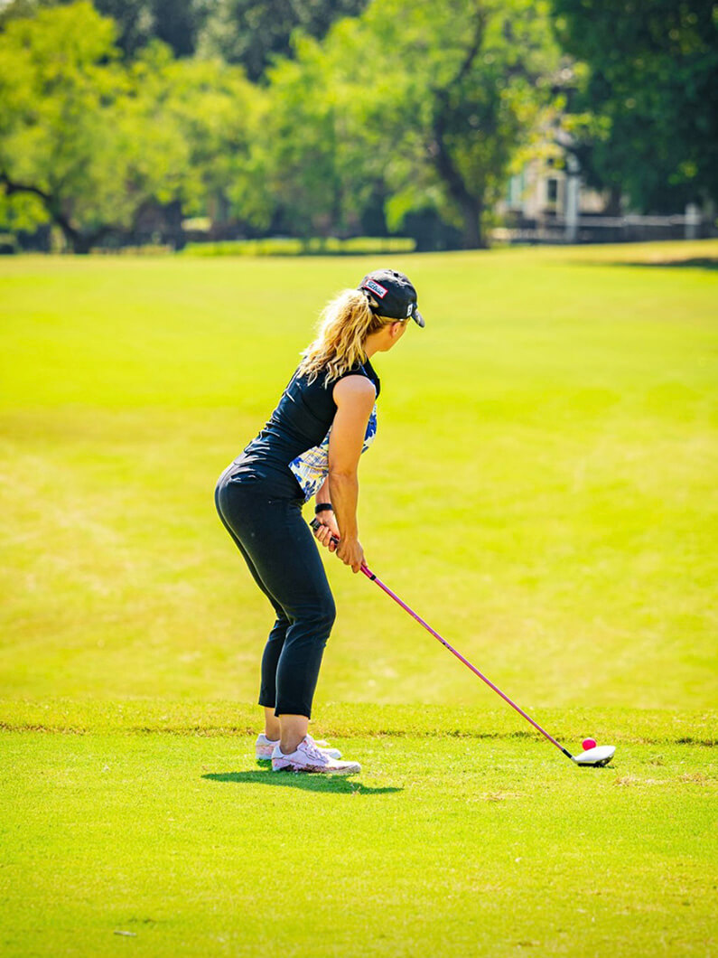 Andrea preparing to tee off on a golf course in sunny weather.