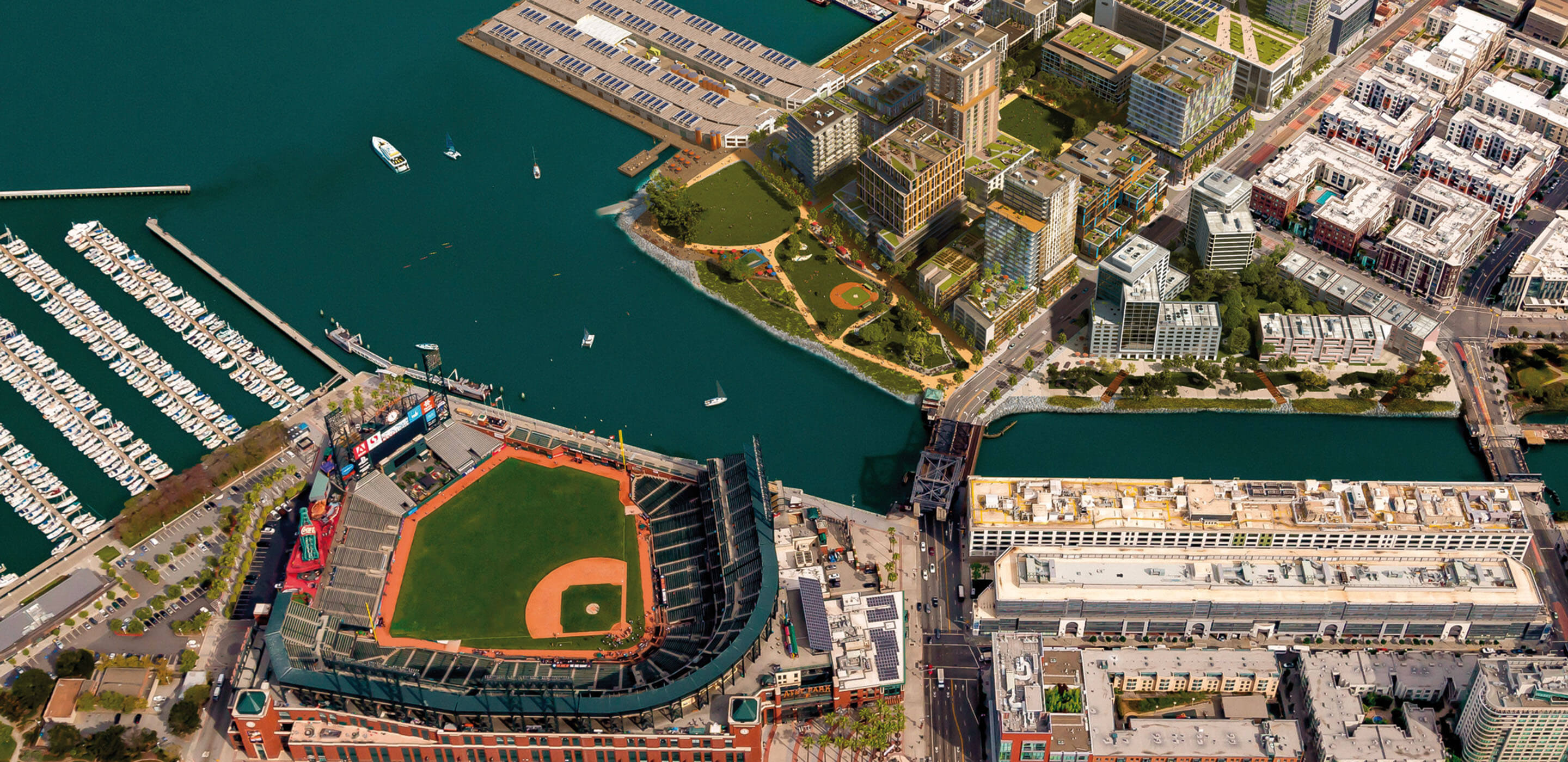 Aerial view of a waterfront area featuring a baseball stadium, residential buildings, a marina, and landscaped parks along the water's edge.
