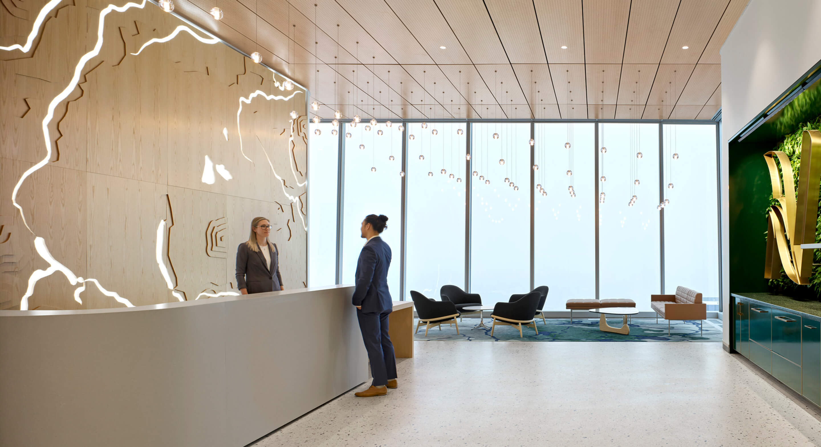 Reception area featuring a woman interacting with a visitor at a sleek front desk, large windows, and contemporary seating arrangements.