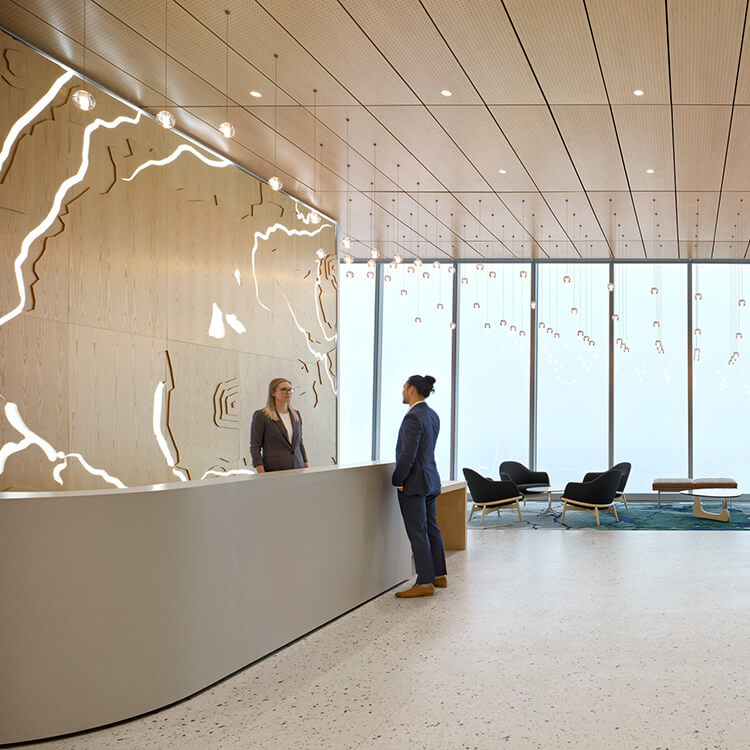 Reception area with two people engaged in conversation. Features wood paneling, intricate wall design, large windows, and stylish seating.