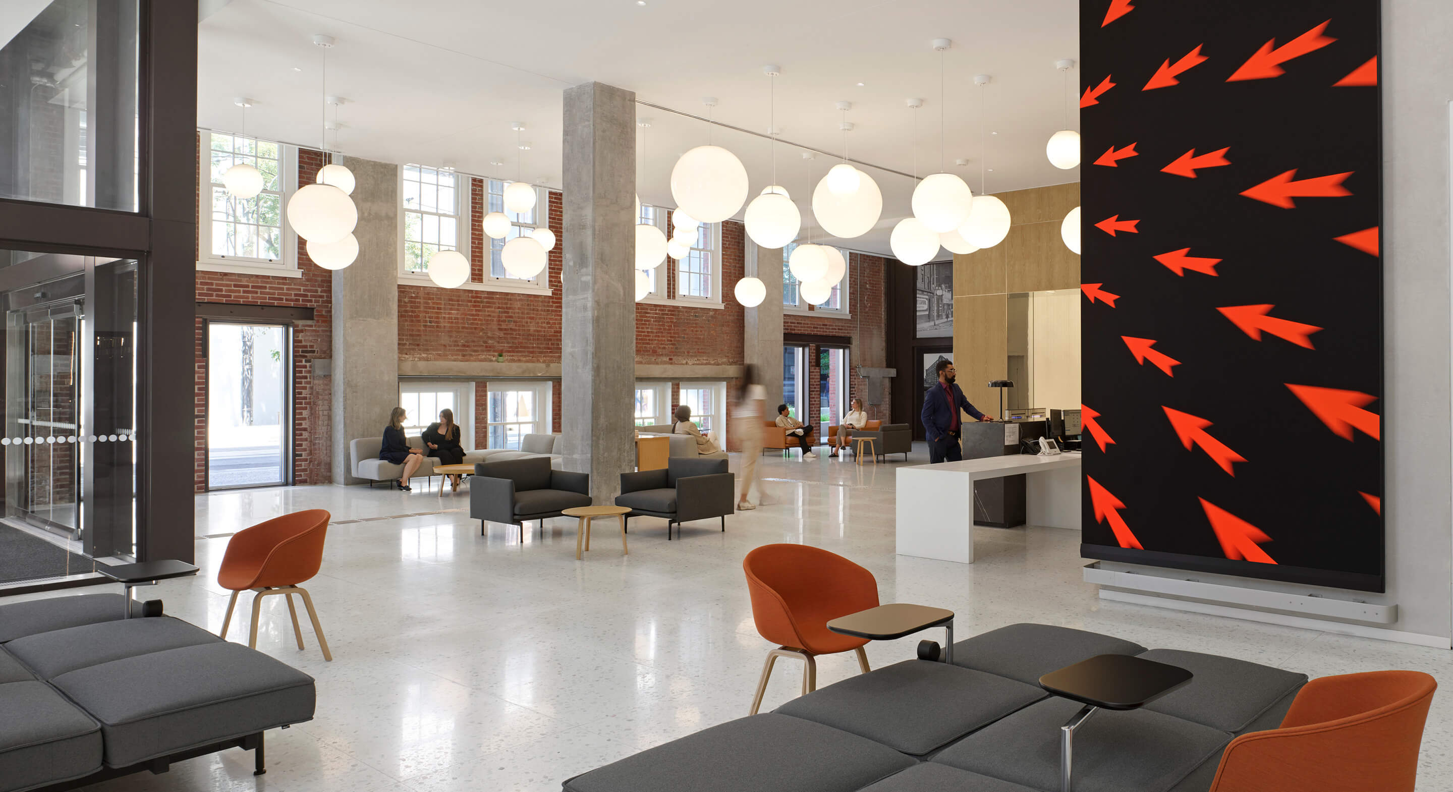Bright lobby featuring distinct furniture, large hanging lights, and a striking wall art design with arrows. People are engaged in conversation.