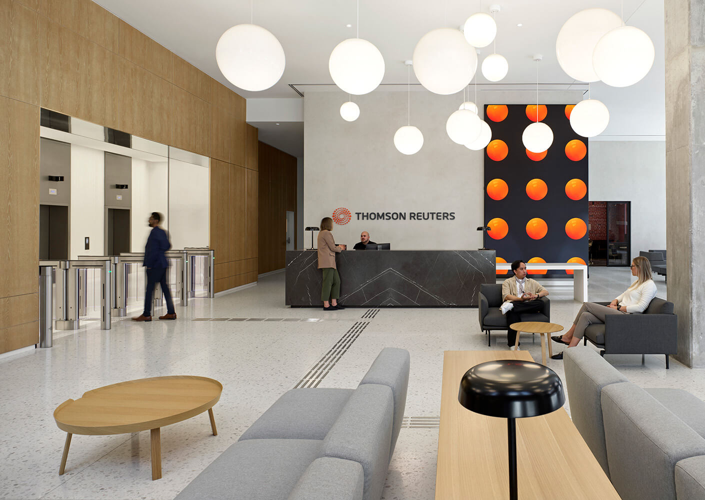 Reception area of Thomson Reuters featuring sleek elevators, a stone reception desk, seating areas, and decorative lighting.