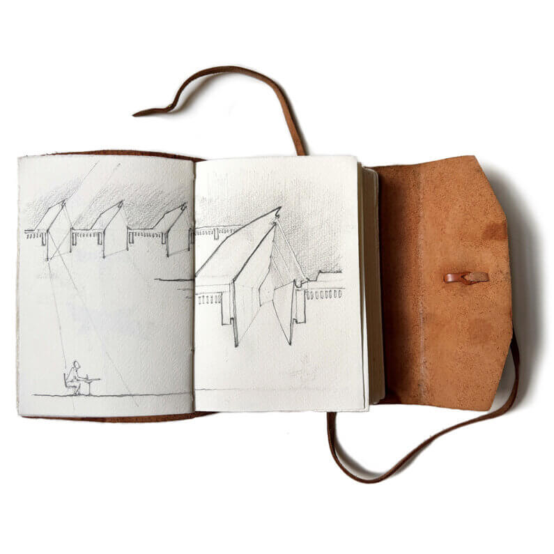 Sketchbook opened to architectural drawings, featuring various building forms and a figure sketching. Leather cover with a tie closure.