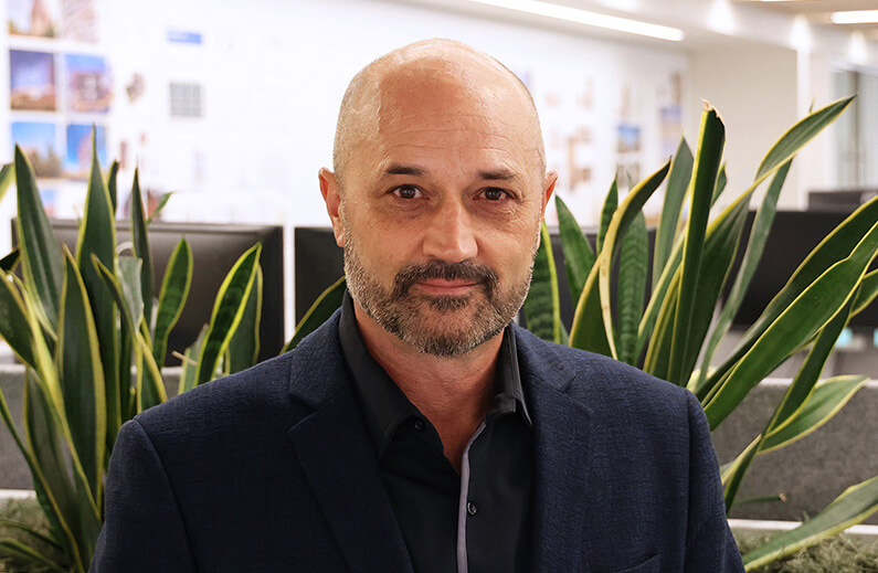 Portrait of a professional in an architectural office, surrounded by plant life and design visuals, highlighting a workspace focused on architecture.