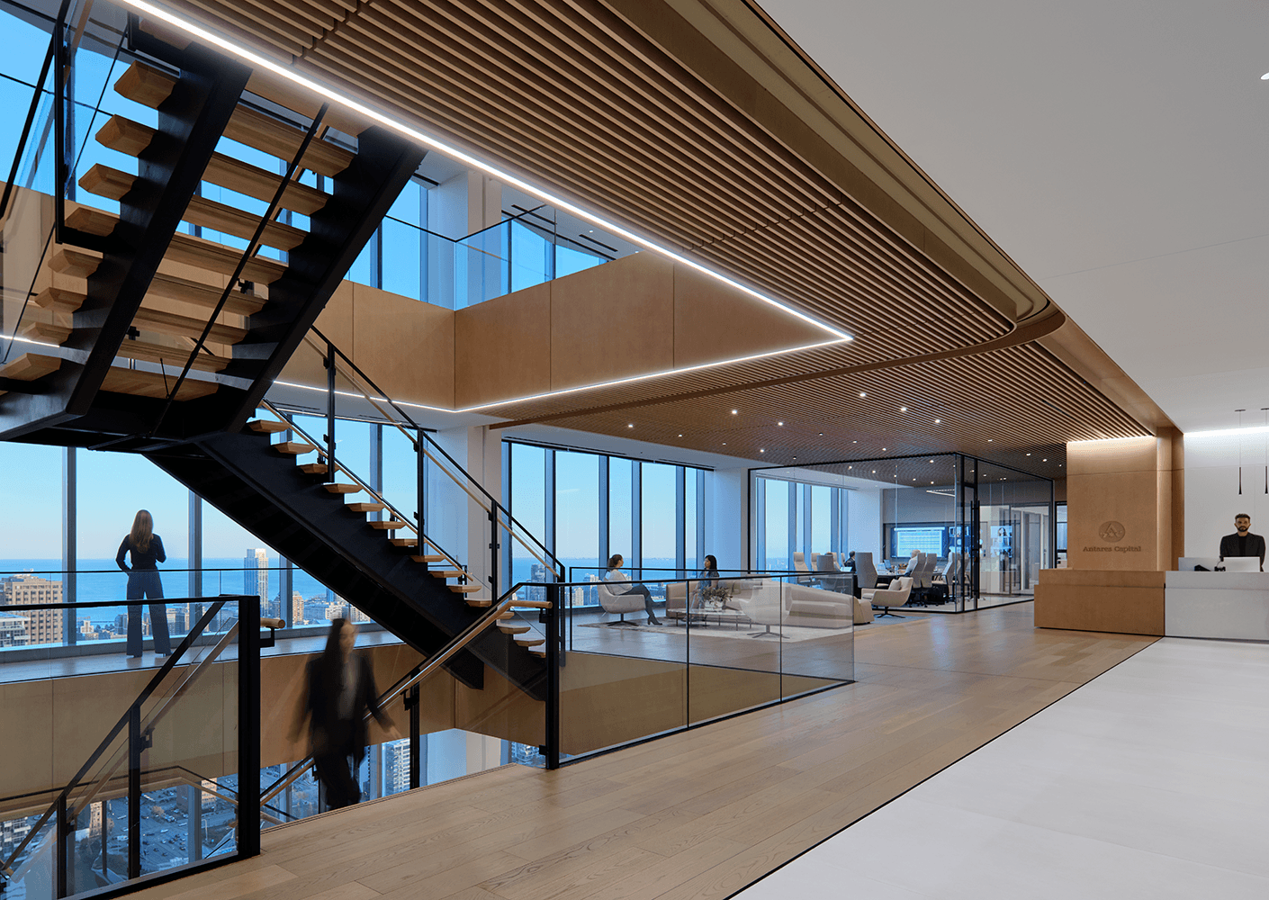 Office interior featuring a two-level space with a glass staircase, large windows, and seating areas for collaboration and work.