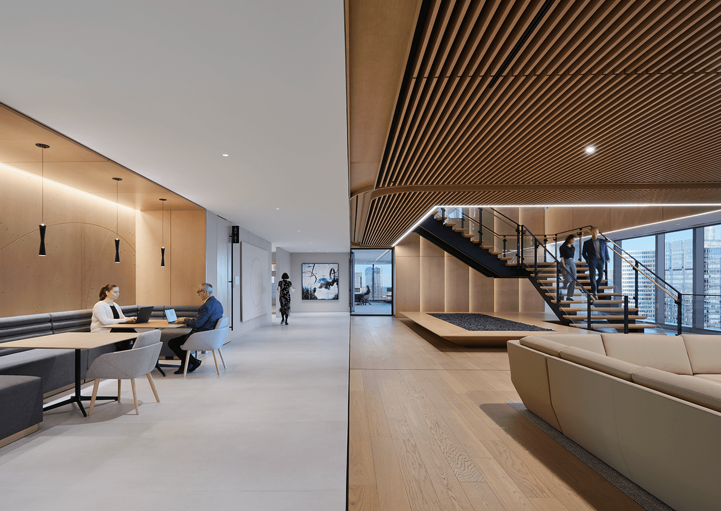 Stylish office interior featuring a collaborative workspace, a staircase, and large windows with city views. Two individuals are using laptops.