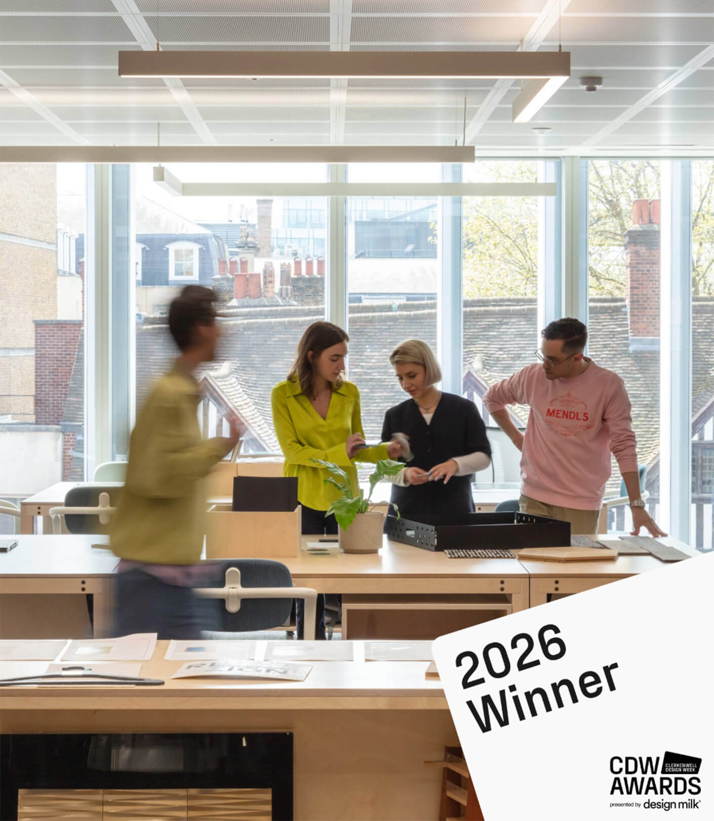 Four individuals collaborate at a workspace with large windows and minimalistic furniture, discussing design materials. 2026 CDW Awards Winner displayed.