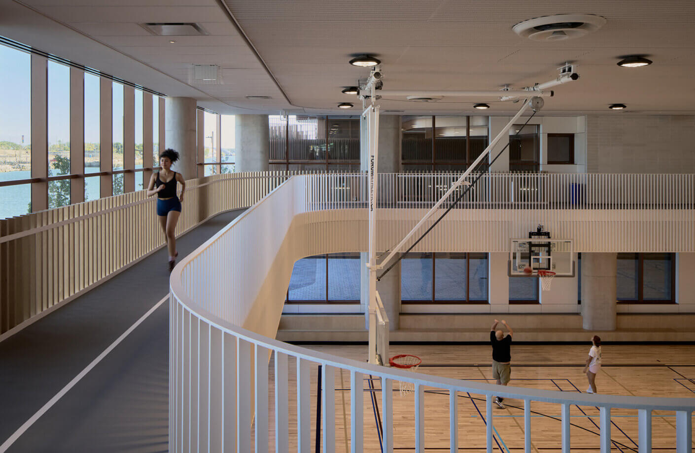 Indoor sports facility featuring a running track, basketball court, and large windows providing natural light. People engaging in activities.