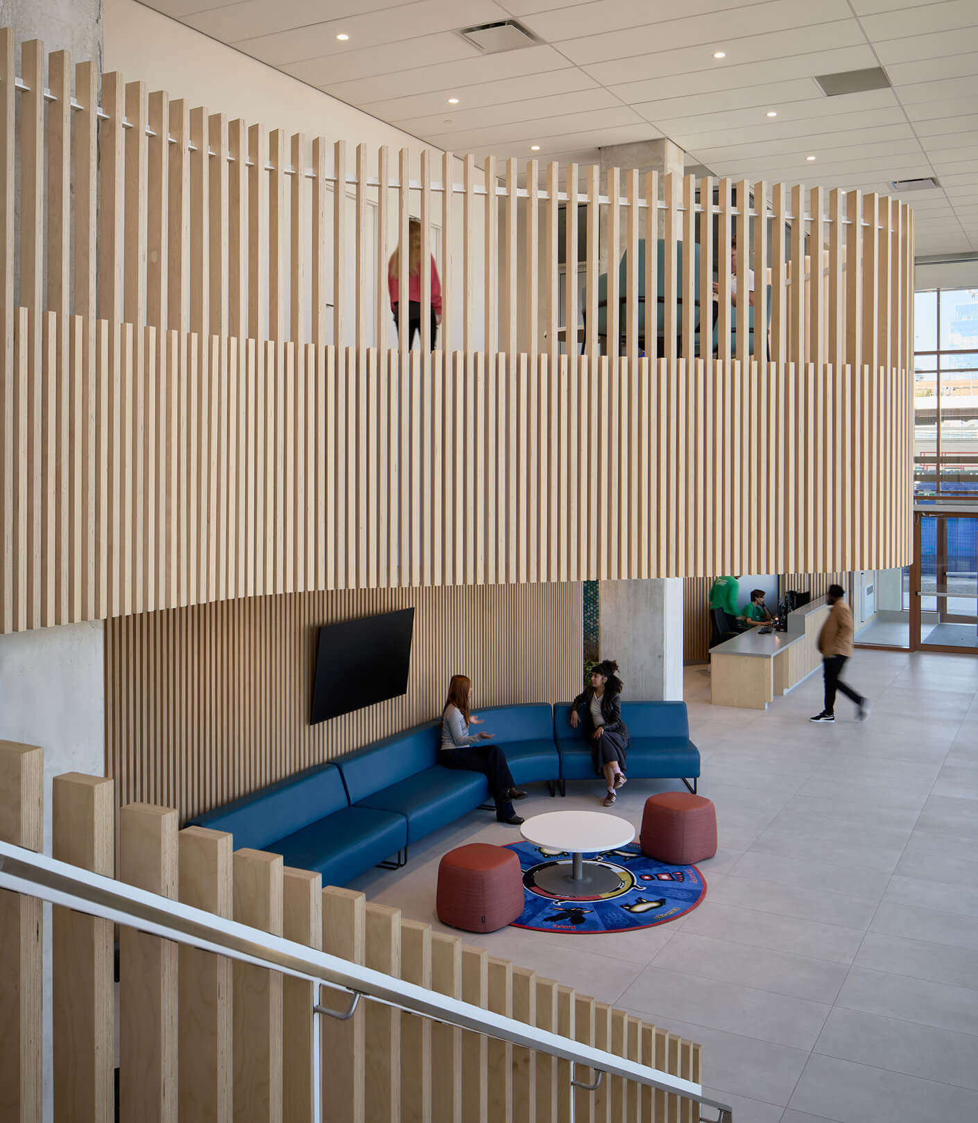 Interior space inside community centre featuring wood paneling, seating areas with blue couches, and people engaging in conversation and movement.
