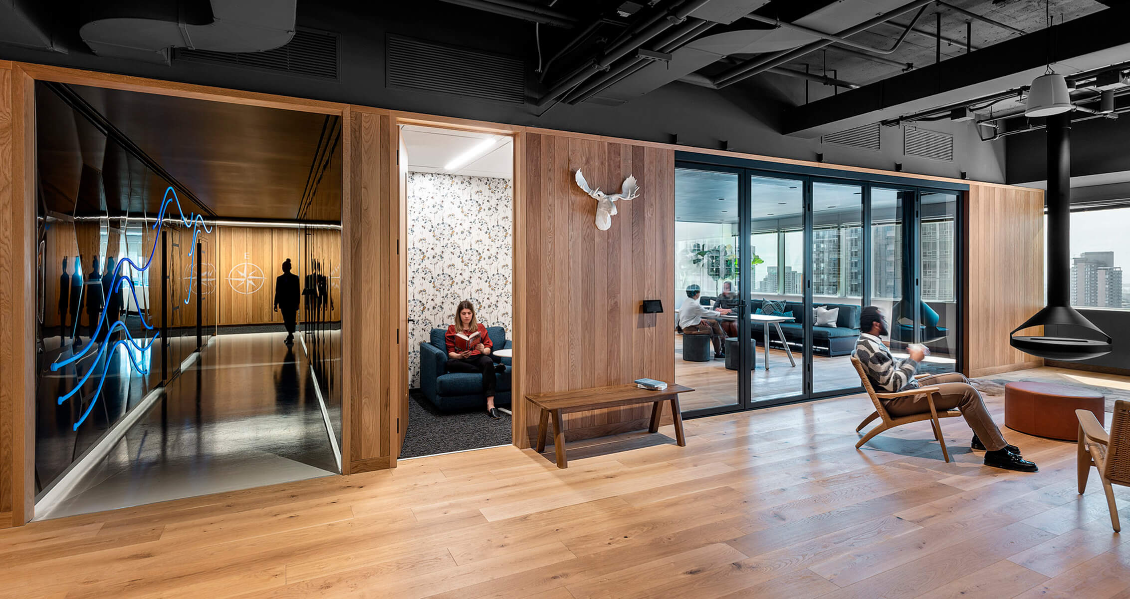 Open office space featuring wooden accents, glass partitions, and modern furniture. People engaged in work and relaxation activities.