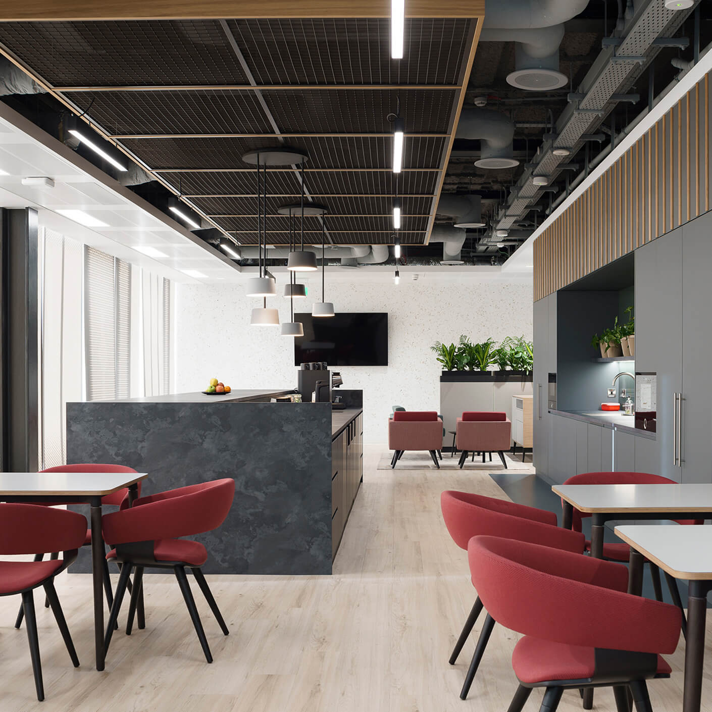Office kitchenette area featuring black countertop, red chairs, and plants. Bright lights illuminate the space, creating a functional workspace.