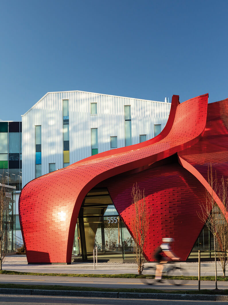 Architectural structure with a striking red facade and unique design, featuring a cyclist in motion on the adjacent street.
