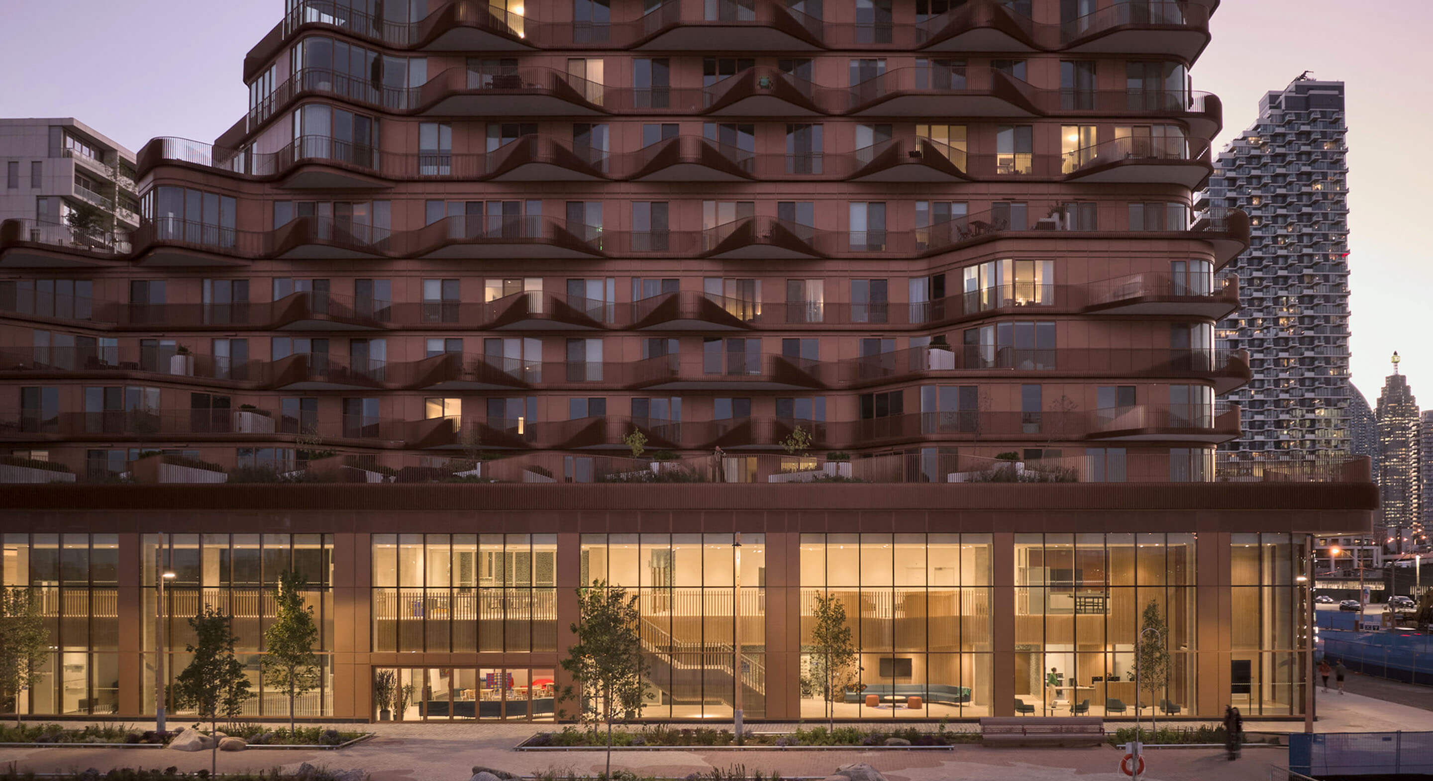 Residential building with unique wave-like design, featuring large glass windows and a landscaped exterior in an urban setting during twilight.