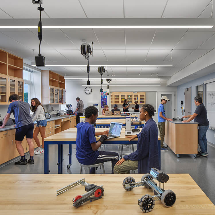 Students collaborating and working on projects in a well-equipped classroom featuring workbenches and various educational tools.