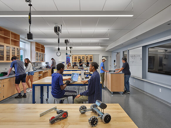 Students engage in hands-on learning in a classroom with workstations, robotics kits, and technology displays. Tables promote collaboration and creativity.