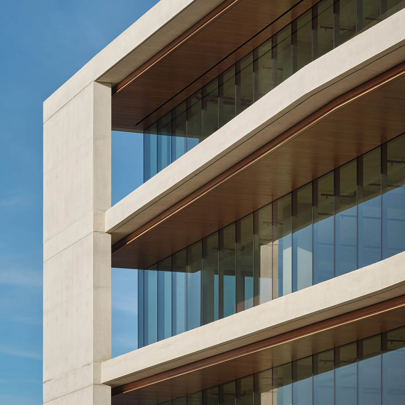 Architectural detail of a building showcasing concrete and glass elements, with wooden accents and blue sky in the background.