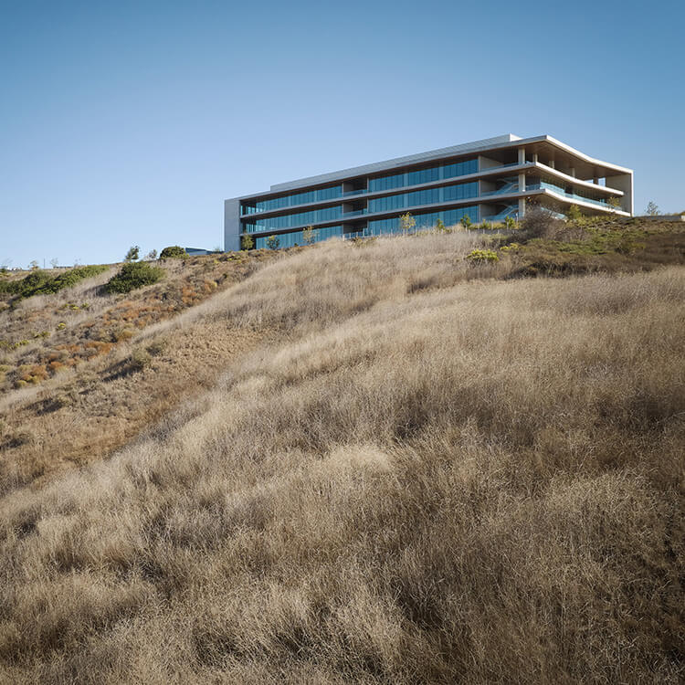 Contemporary building on a hillside, surrounded by dry grass and sparse vegetation under a clear blue sky.