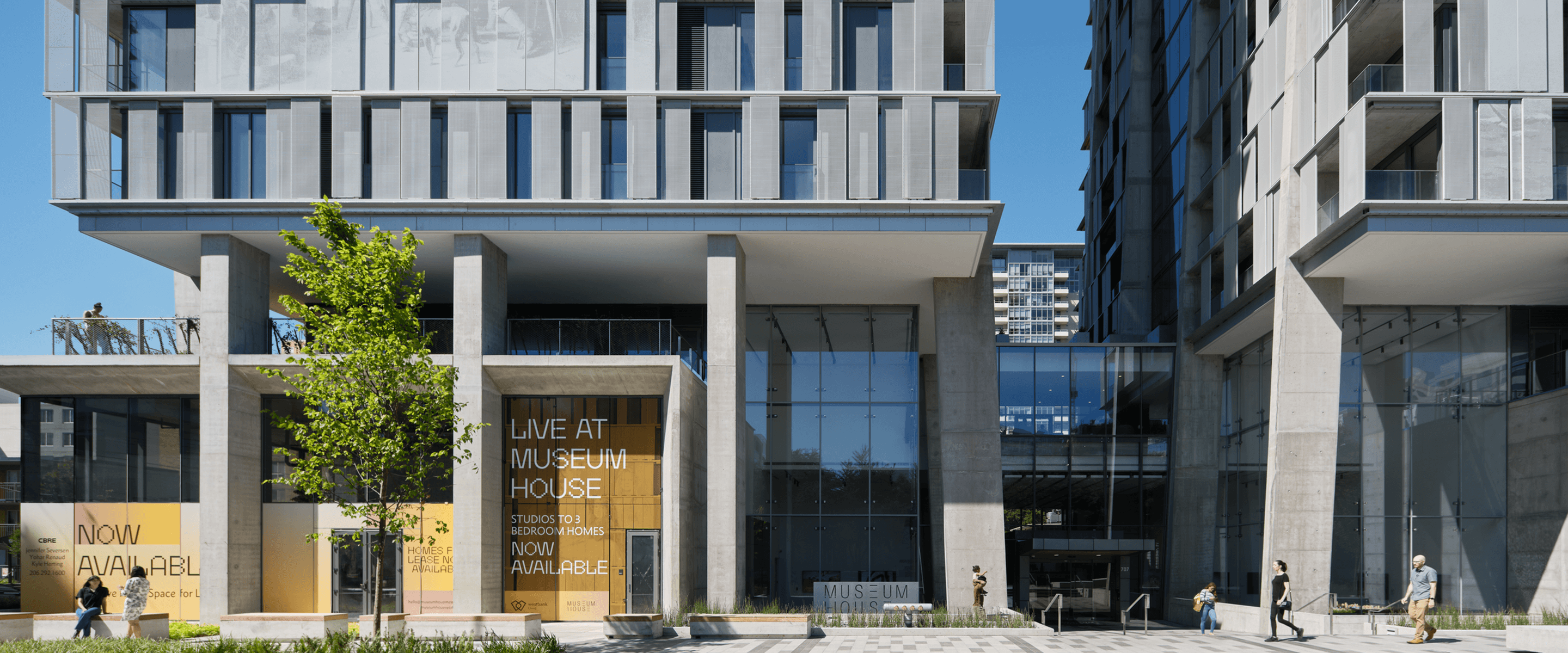 Exterior view of Museum House, featuring a glass façade, concrete structure, and a sign indicating available studio and one to three-bedroom homes.