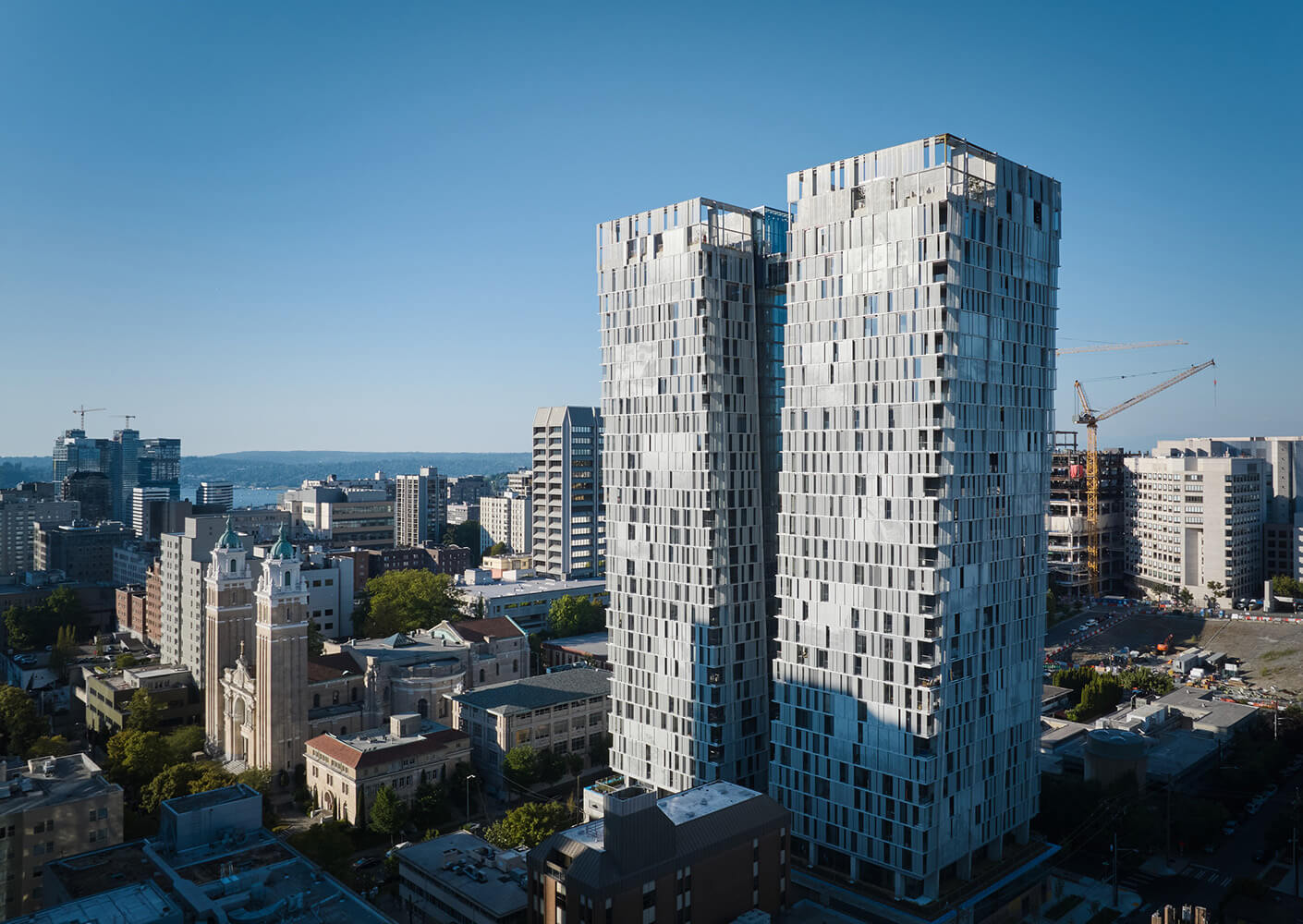 Aerial view of two high-rise buildings in an urban landscape, with construction sites and historical architecture in the foreground.