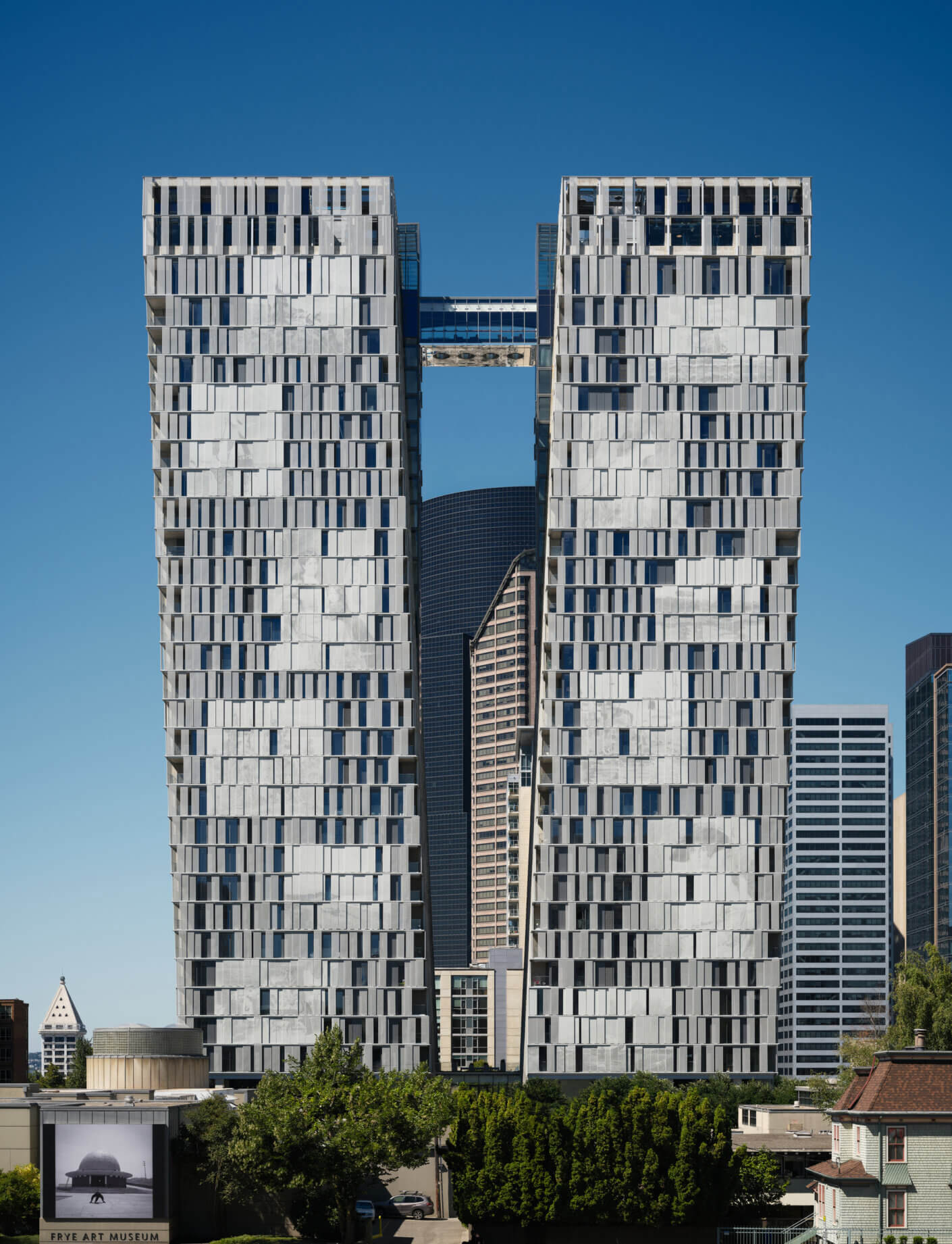 Two towers with unique facades stand against a clear blue sky, featuring a distinctive gap and varied window designs in an urban setting.