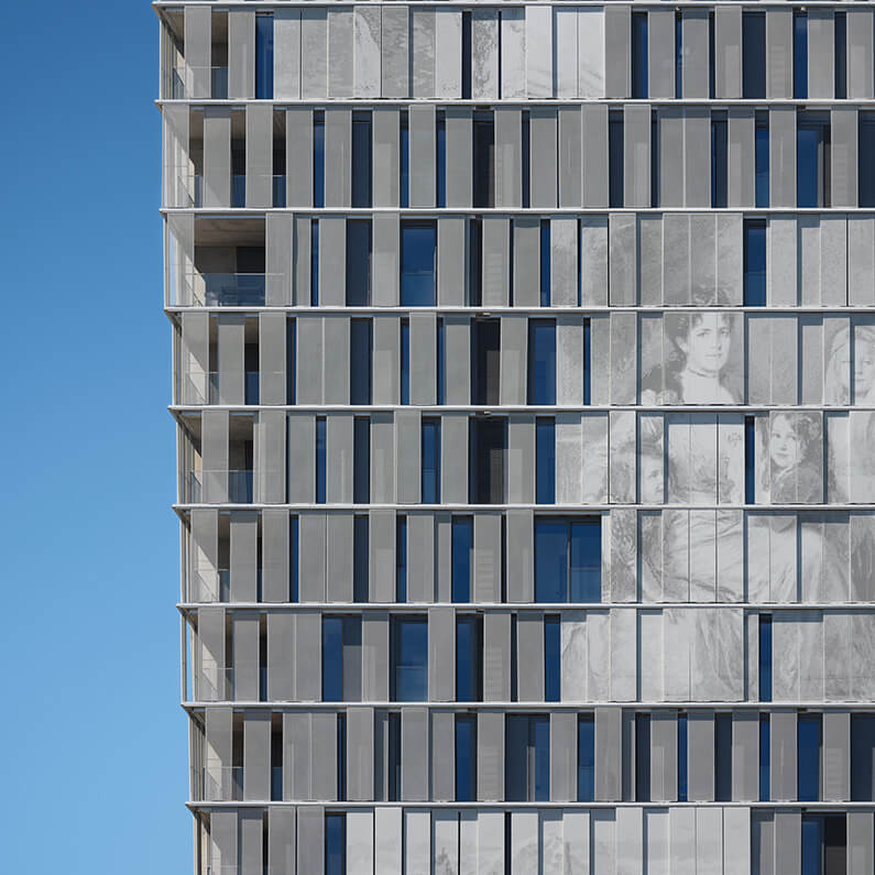 Facade of a multi-story building featuring vertical slats and large windows, with photo art integrated into the design. Clear blue sky in the background.