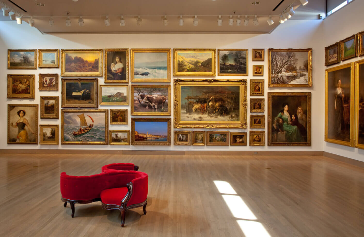 Art gallery interior showcasing a variety of framed artworks on the walls, with a red velvet chair positioned in the foreground.
