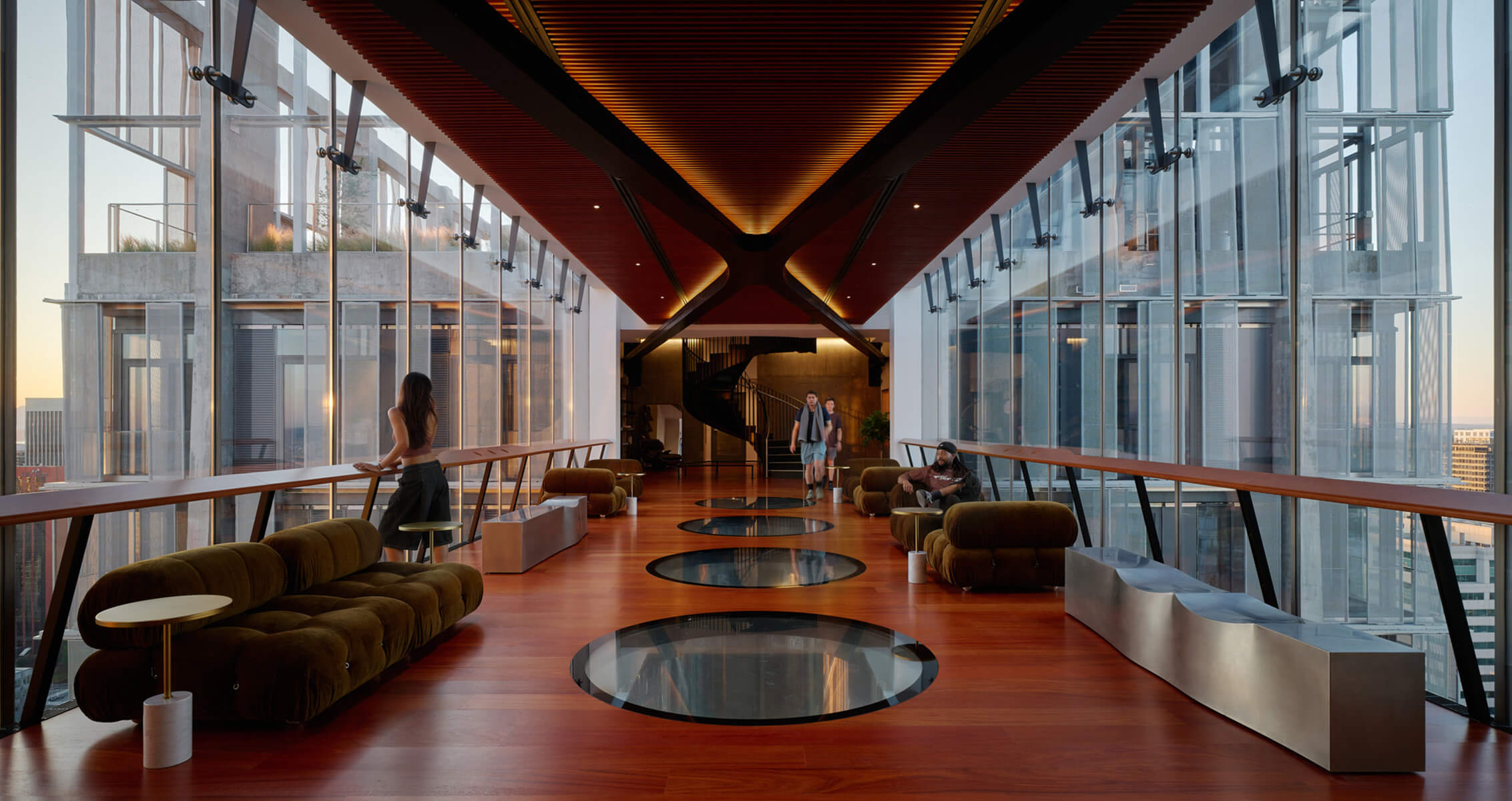 Stylish interior space with large glass windows, wooden flooring, and contemporary seating. People engage in conversation and relaxation.
