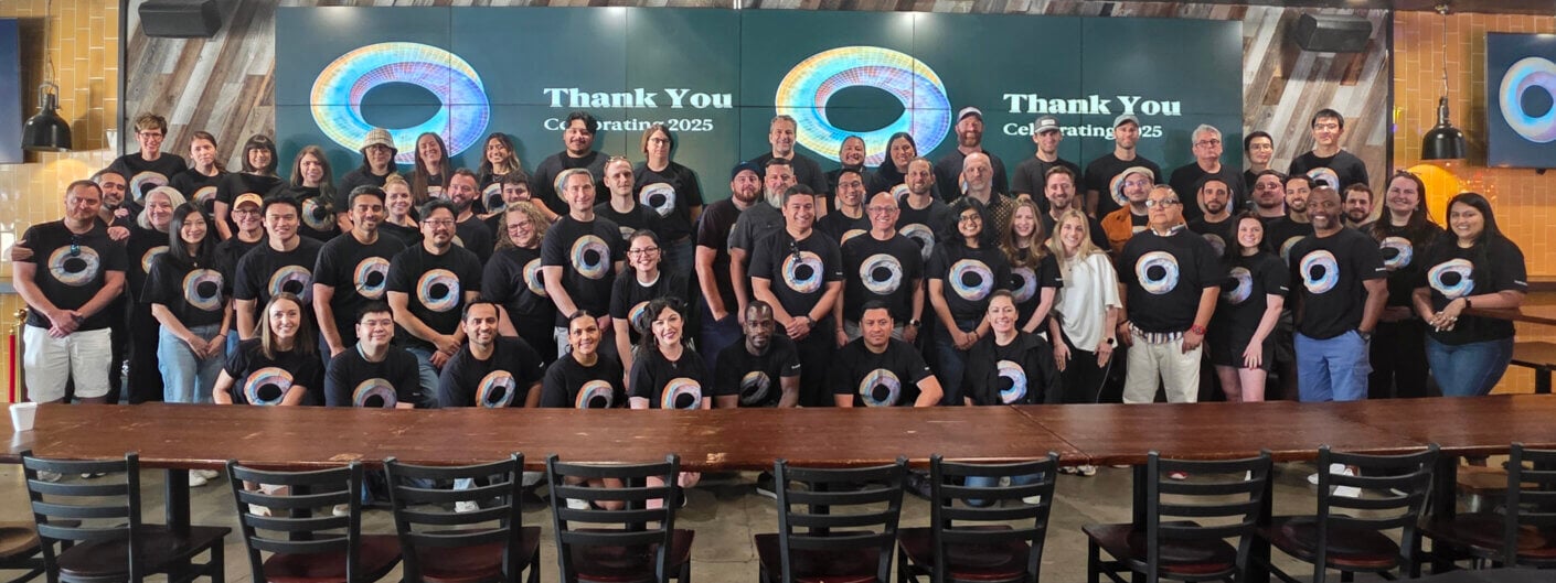 Group photo of a team celebrating an event in matching black t-shirts, with a Thank You and Celebrating 2025 display in the background.