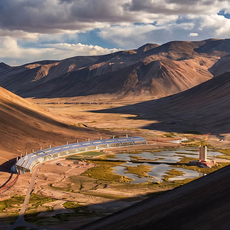 Aerial view of an architectural structure along a curved road, surrounded by mountains and water bodies in a desert landscape.