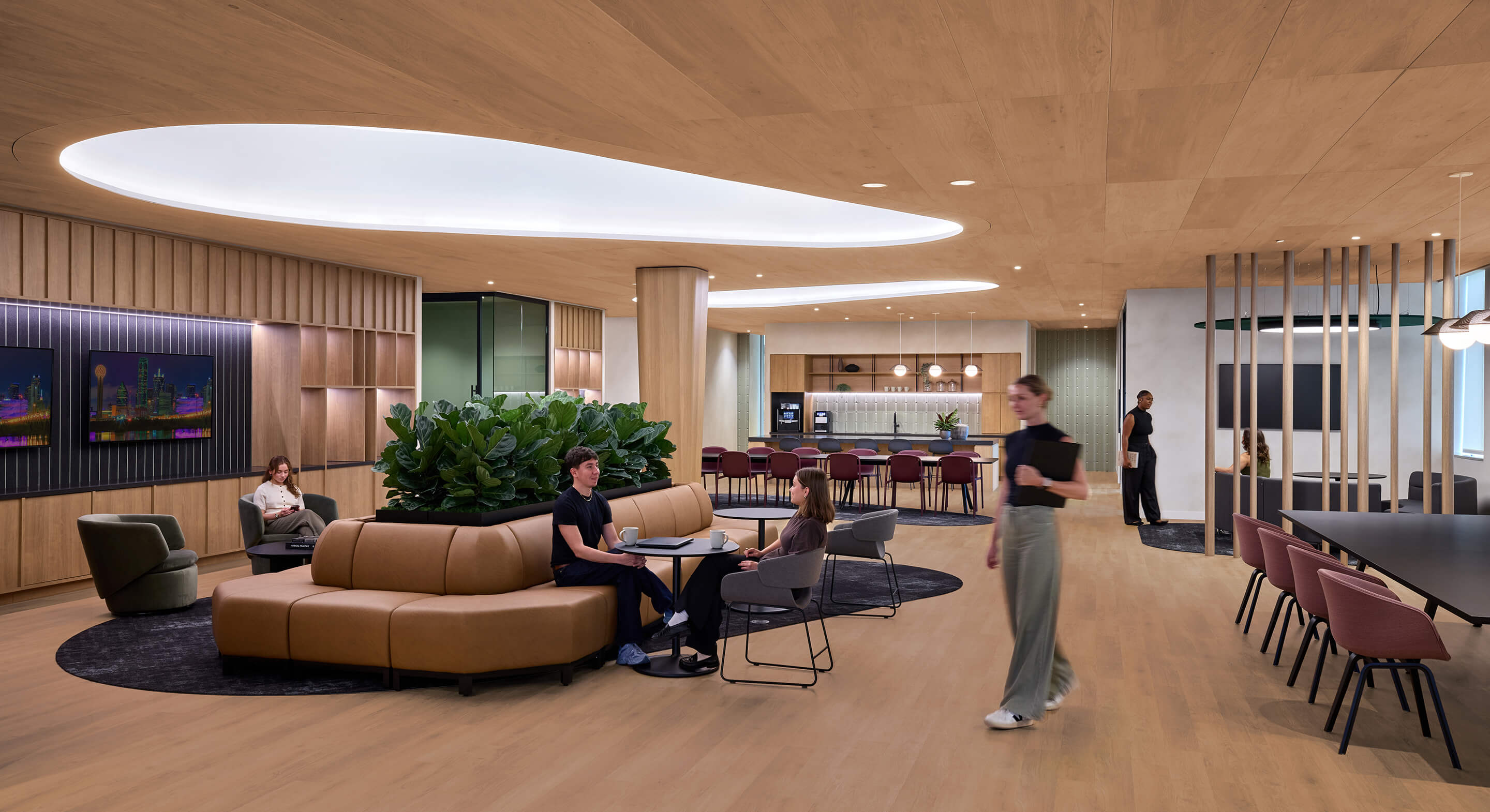 Interior view of a collaboration space featuring seating areas, plants, and a kitchenette, with people engaging and working throughout the setting.
