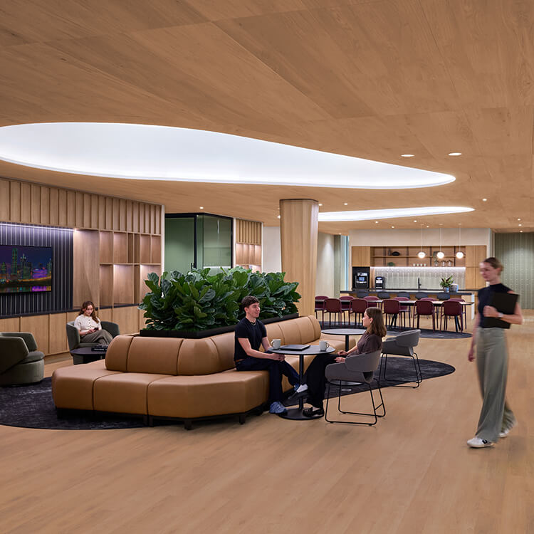 Bright interior space featuring seating areas, greenery, and a kitchenette. People are engaged in conversation and casual activities.