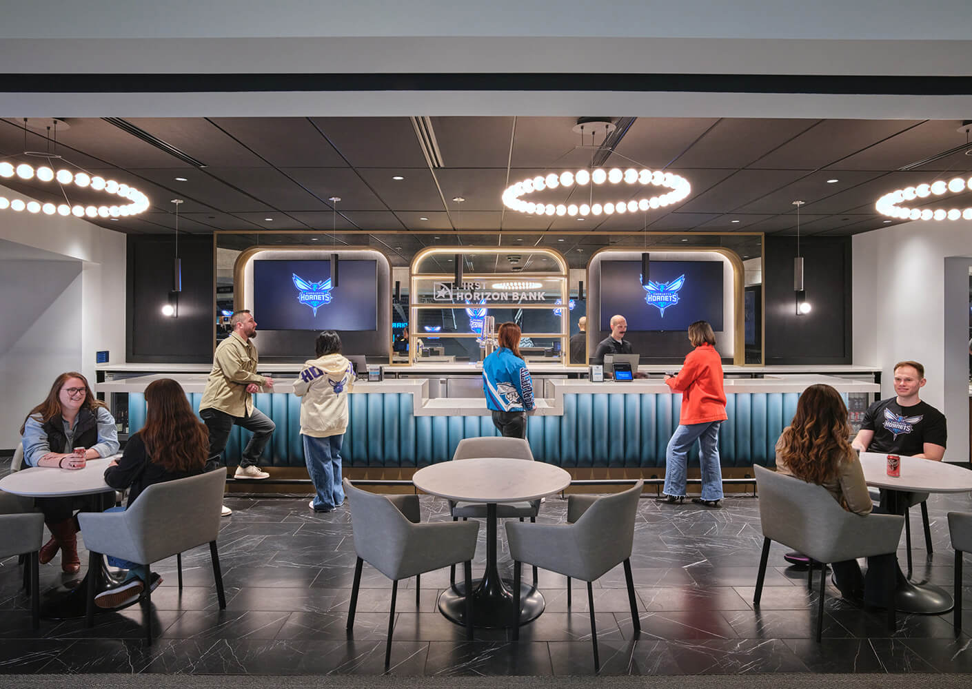 Bank interior with customer interactions at the counter, featuring two screens displaying the Hornets logo and modern seating arrangements.