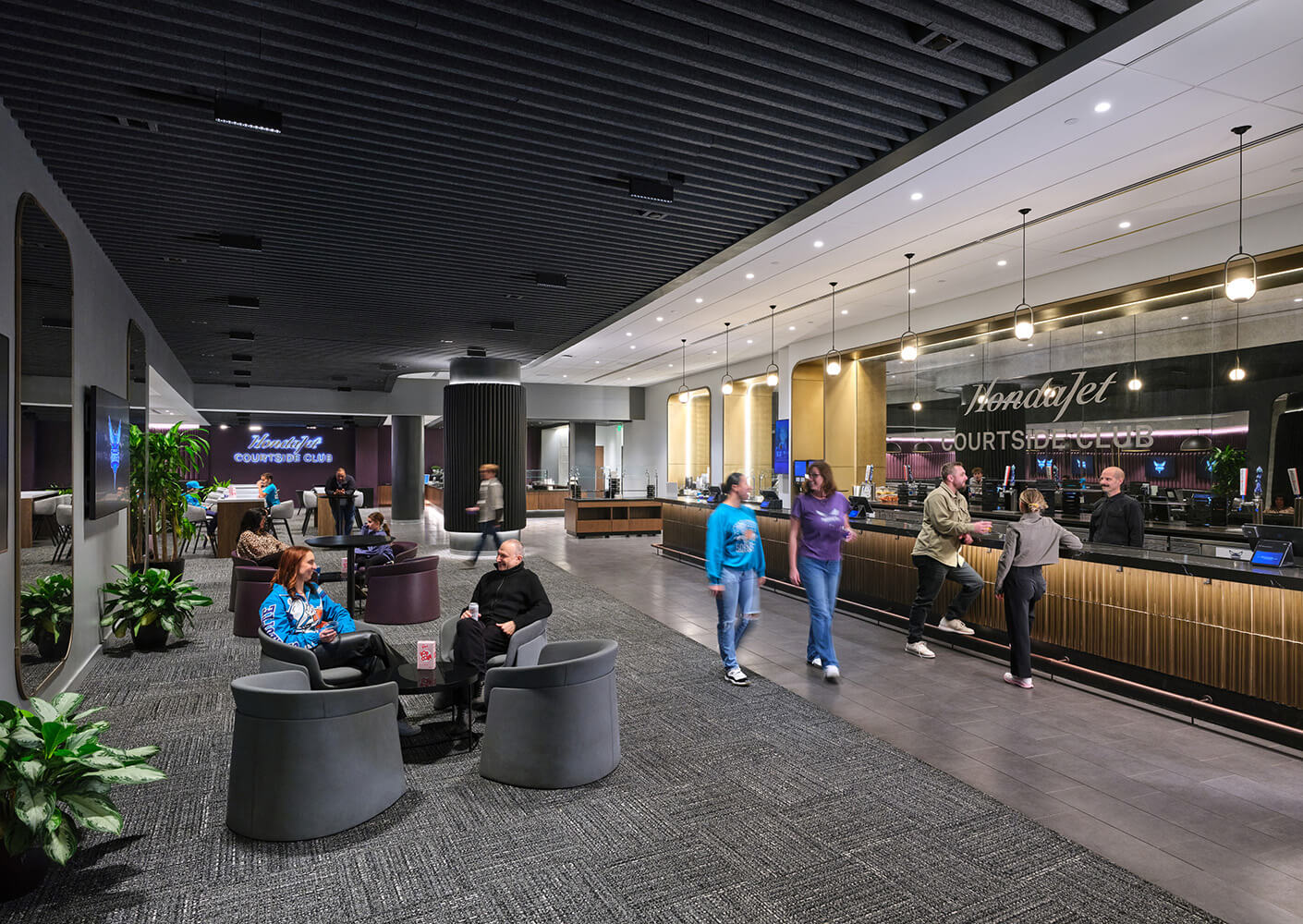 Interior view of the HondaJet Courtside Club, featuring seating areas and a bar. People mingle and interact in a spacious environment.