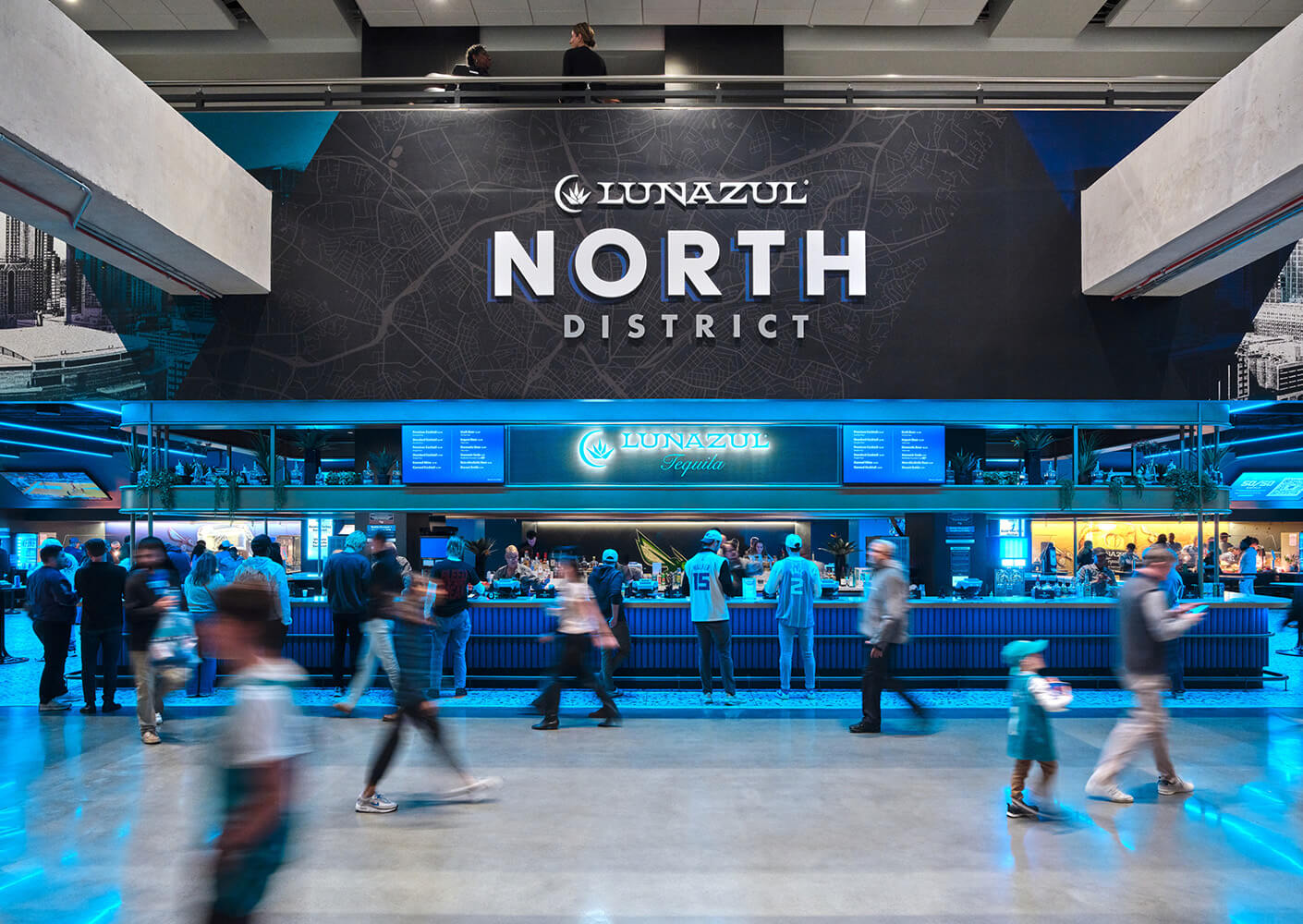 Crowded venue interior with a large NORTH DISTRICT sign and a bar serving Lunazul Tequila, showcasing visitors engaged in various activities.