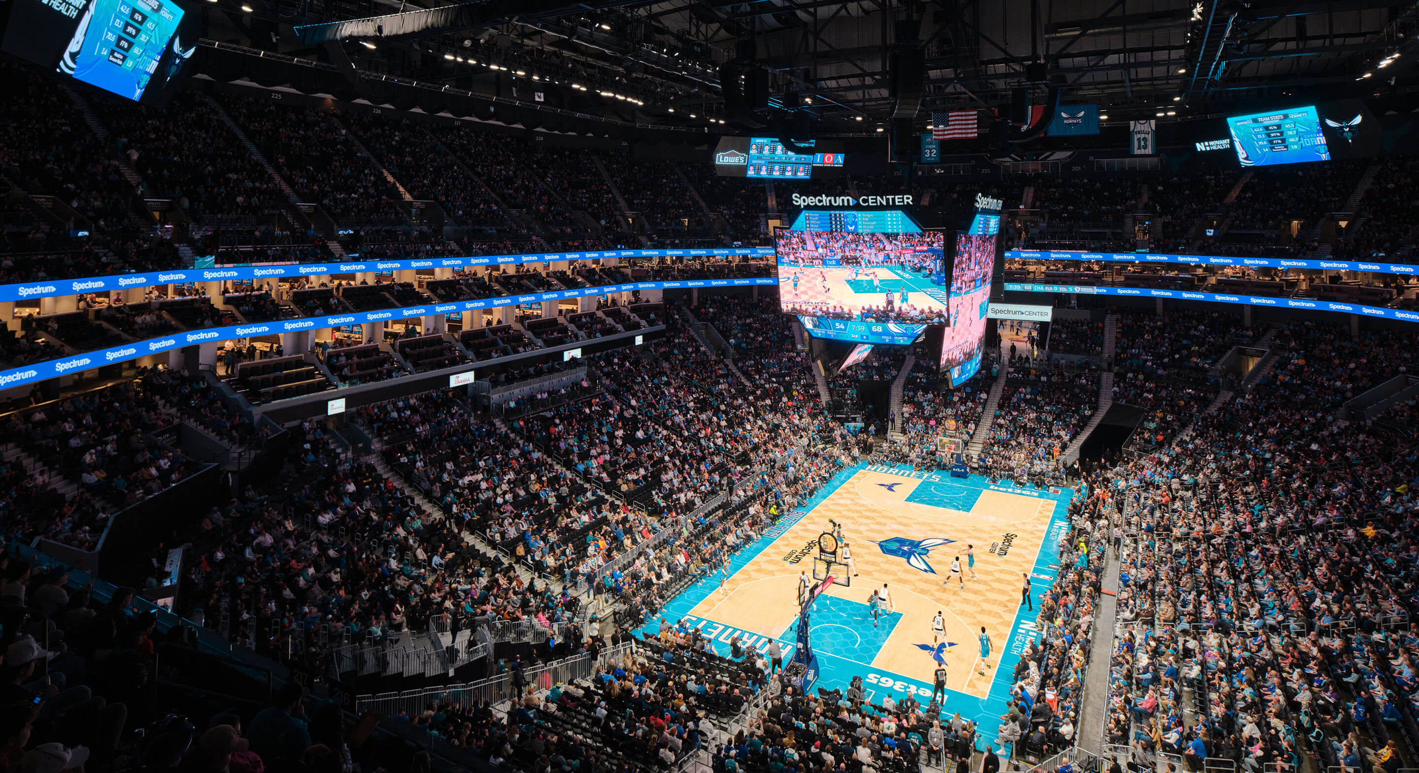 High-angle view of Spectrum Center during a basketball game, showcasing a packed crowd, vibrant court, and large scoreboard.