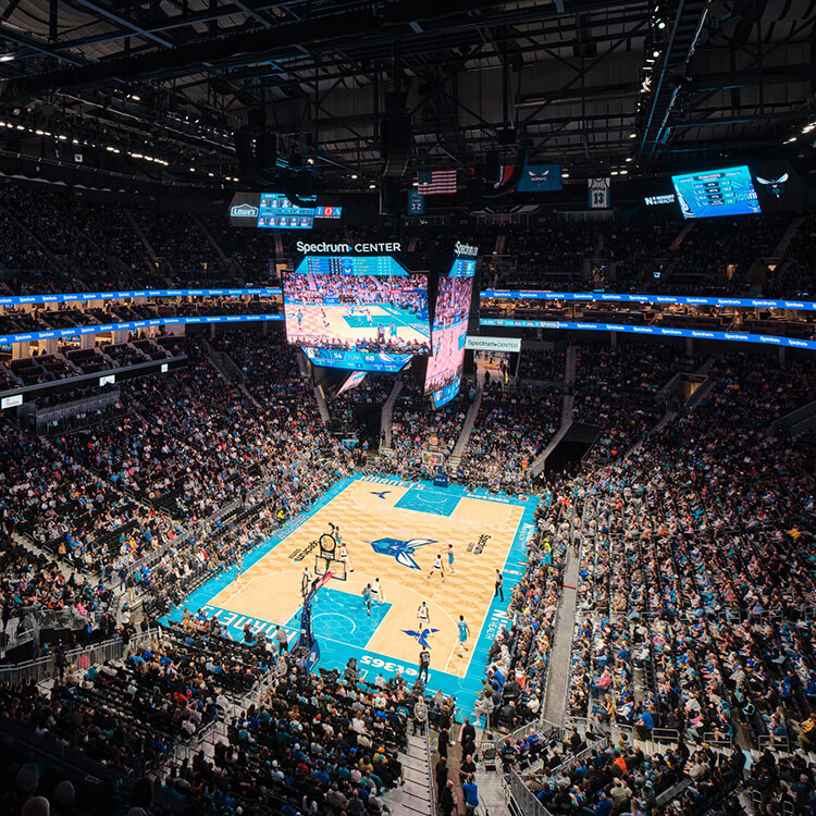 Basketball game in progress at Spectrum Center, with a packed crowd and large screens displaying the action on the court.