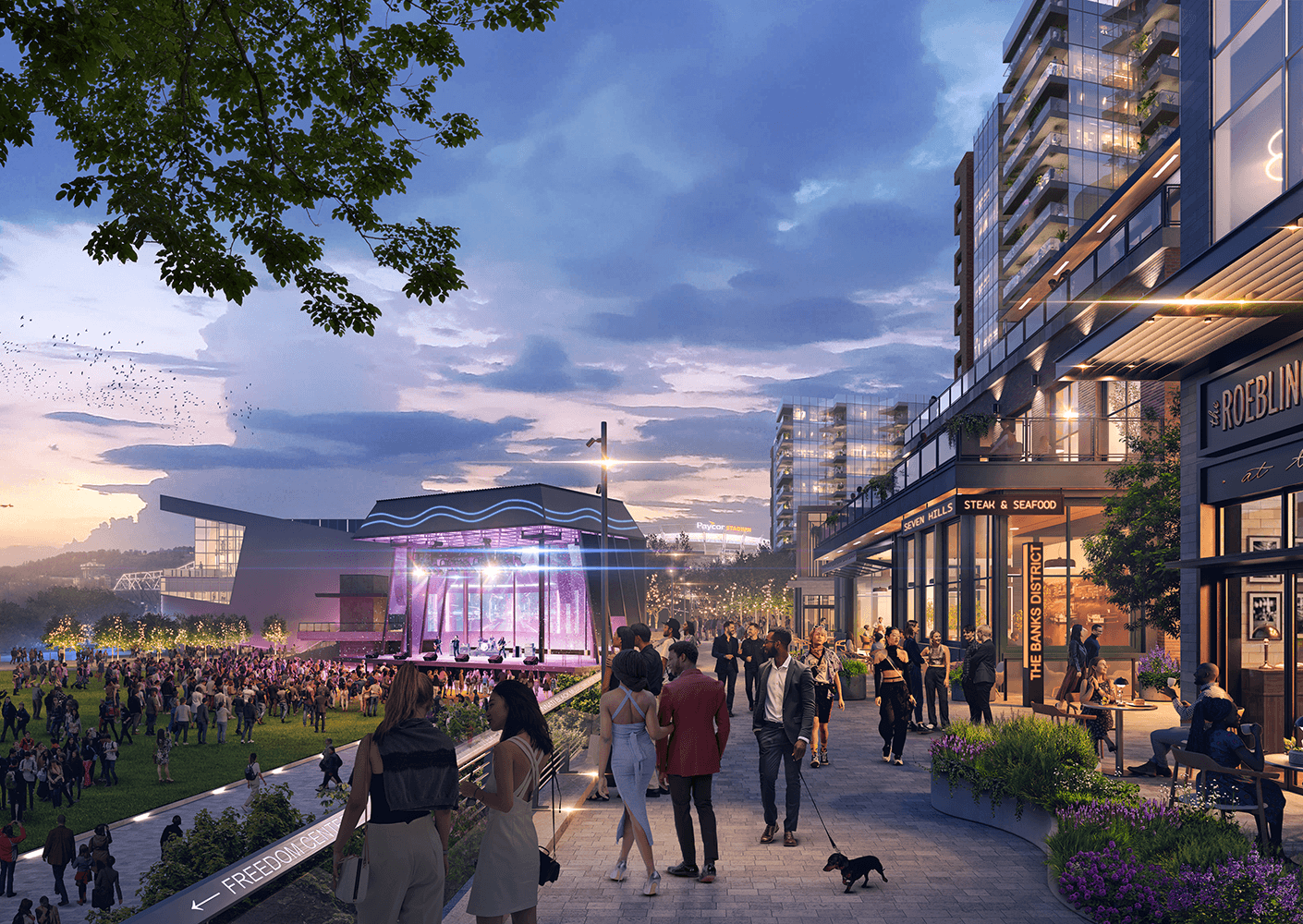 Crowd enjoying an outdoor concert near restaurants and shops, with modern buildings and greenery in the background during twilight.