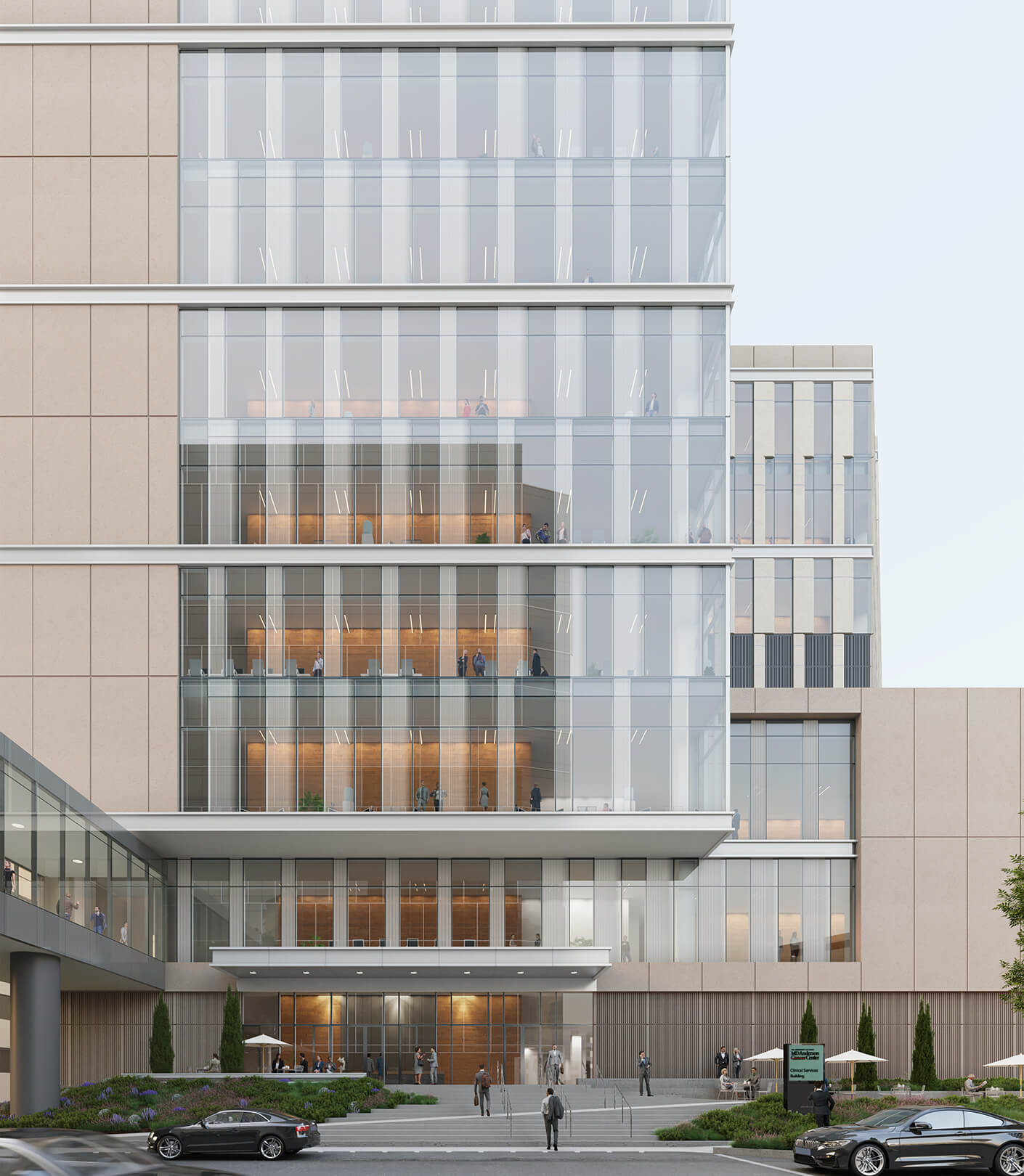 Exterior view of a multi-story building with glass facades, featuring balconies, outdoor seating, and landscaping at the entrance.