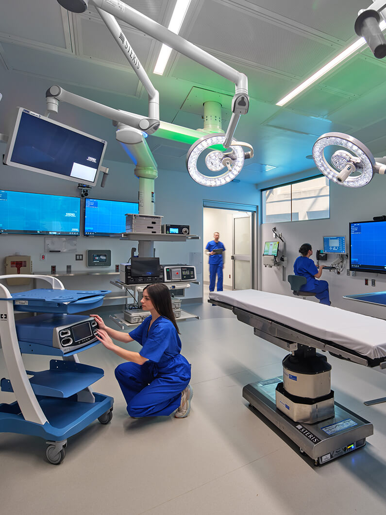 Healthcare professionals in blue scrubs work in a surgical room equipped with advanced medical technology and monitors.