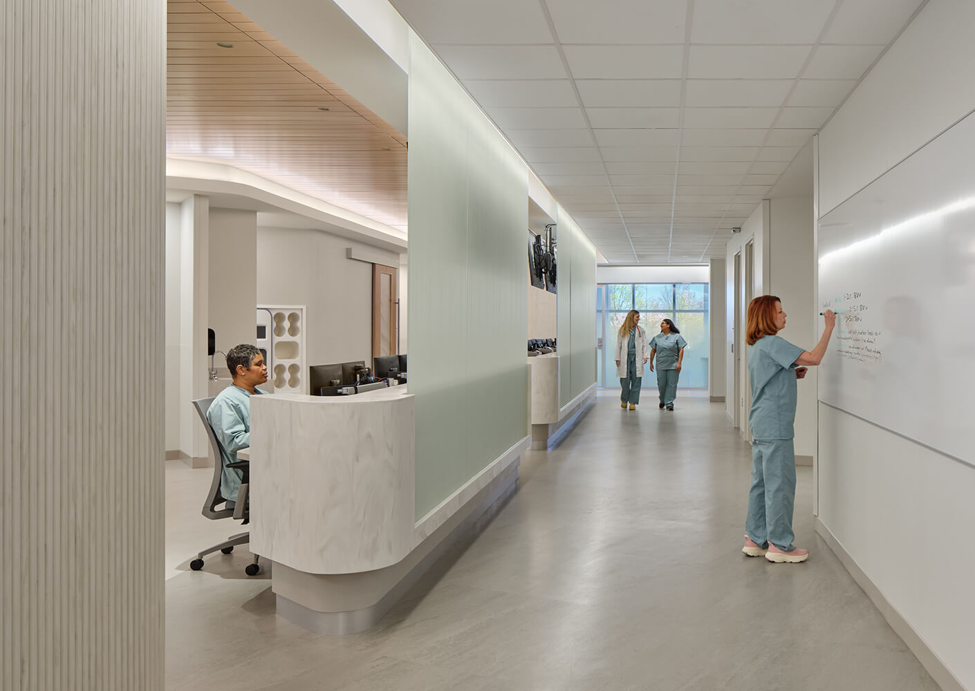 Healthcare professionals in scrubs work in a sleek, well-lit corridor with a reception desk and whiteboard for notes.