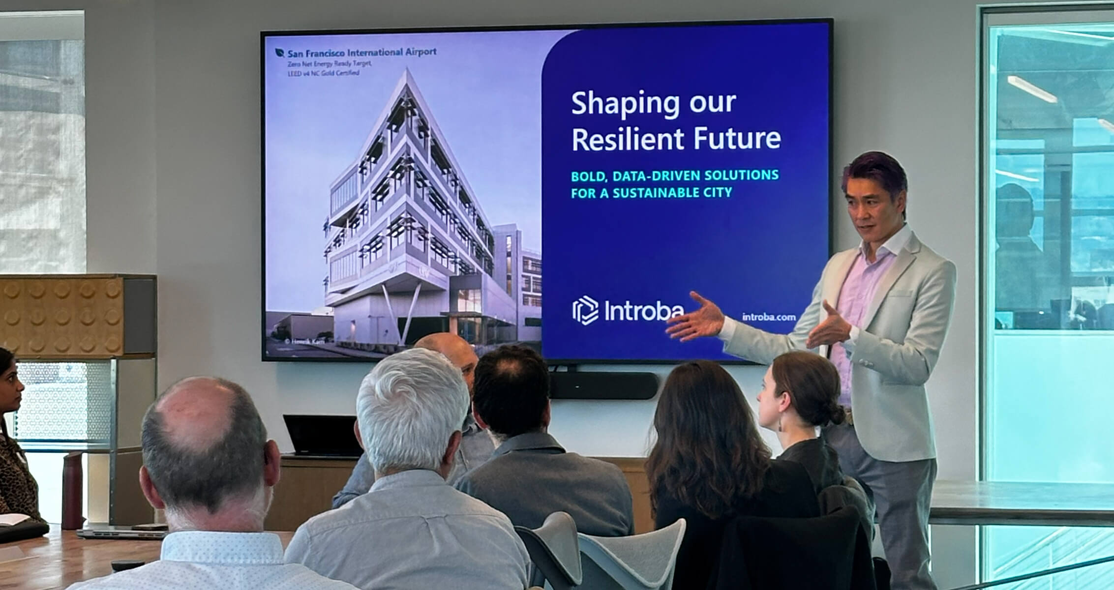 Speaker presents at a meeting about sustainable solutions for San Francisco International Airport, with a project image displayed on a screen.