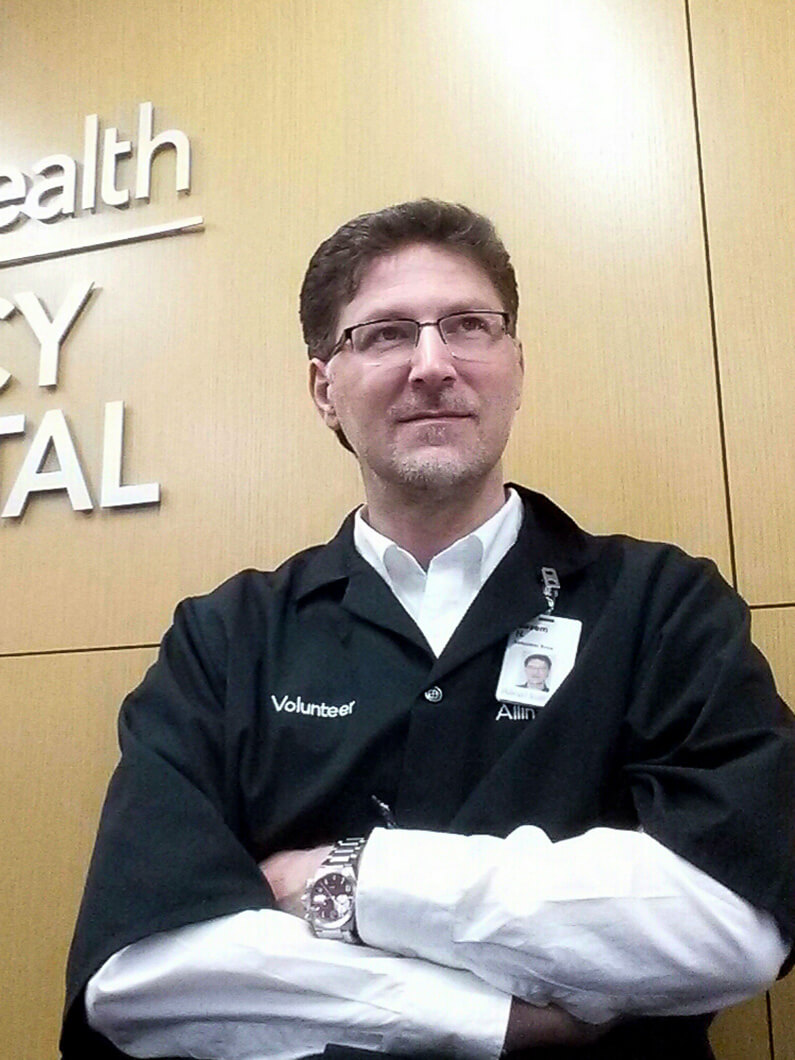 Basem, with a volunteer badge, poses against a hospital wall