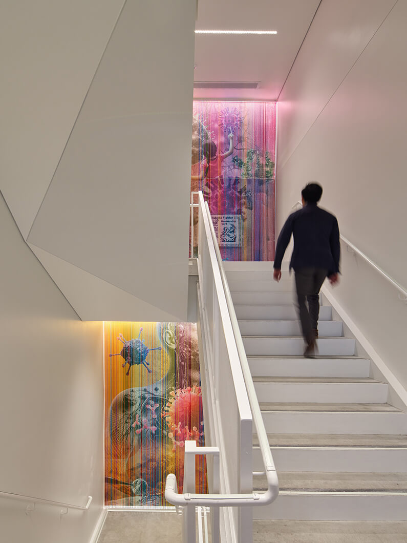 Person walking up a staircase featuring vibrant artwork on the wall, with colorful designs and illuminated accents providing visual interest.