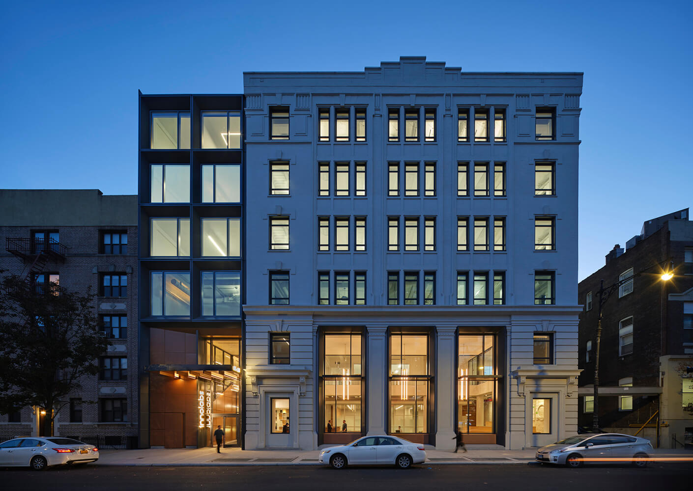 Facade of a commercial building featuring a blend of architectural styles, illuminated windows, and entrance signage at dusk.