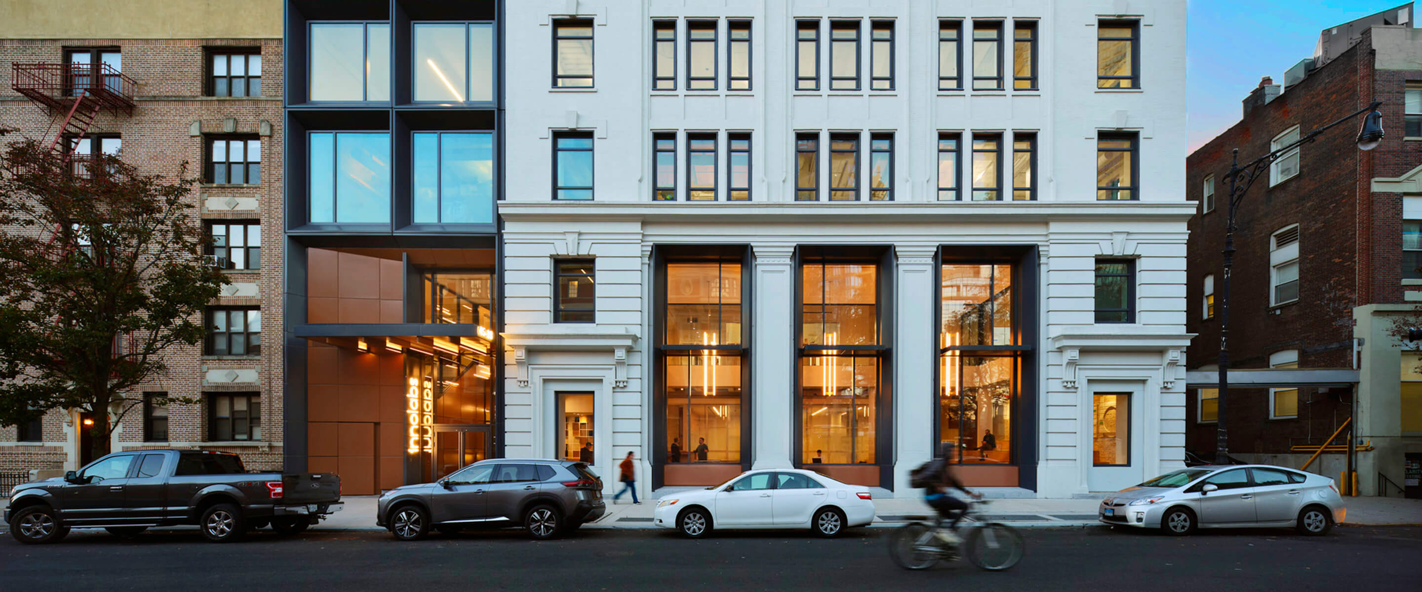 Exterior view of a building featuring a mix of architectural styles, showcasing large windows and an entrance with illuminated signage.
