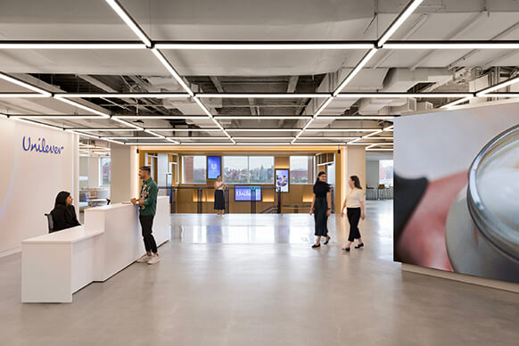 Reception area of Unilever office featuring a front desk, digital displays, and people interacting in a spacious, well-lit environment.