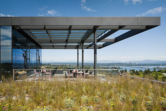 Rooftop terrace with glass walls and a covered seating area overlooking a landscape with greenery and distant mountains.